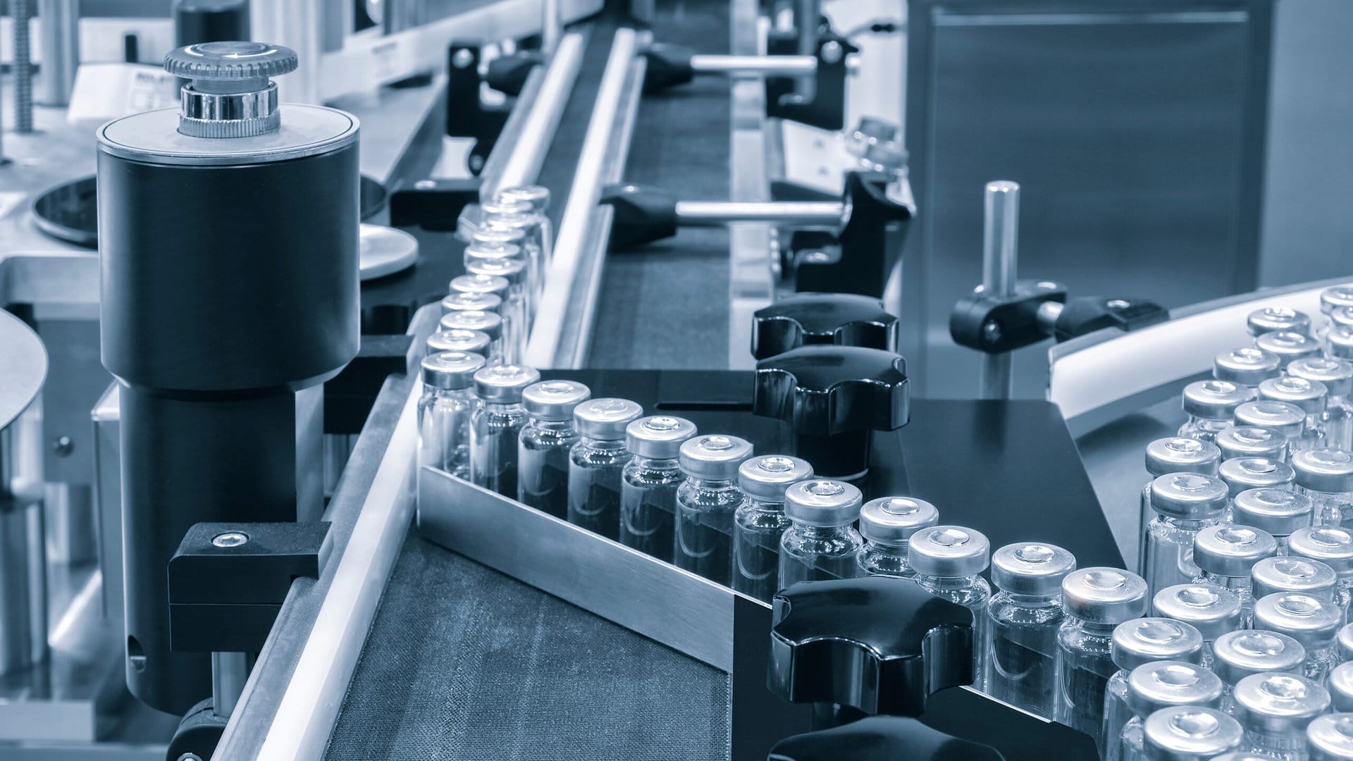 Vials with metal caps move along a conveyor belt in a sterile pharmaceutical production facility, where automated machines and equipment operate within an industrial Unified Namespace (UNS) for seamless data integration.