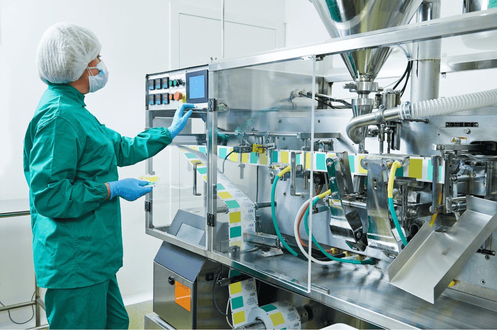 A person in green scrubs and a hairnet operates a packaging machine in a clean, sterile facility. Colorful labels move through the automated system, indicating an industrial production process—demonstrating how Unified Namespace enhances efficiency and traceability within Medizintechnik environments.